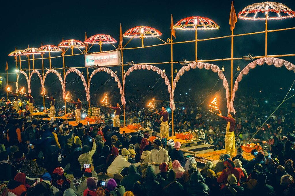 Varanasi evening aarti ceremony: Hindu priests perform ritual with flaming lamps under lit arches, large crowd gathers on Ganges river ghats