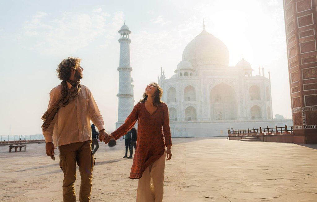 Couple visiting the Taj Mahal in Agra, walking hand in hand with the iconic white marble monument and minaret glowing in soft morning sunlight.