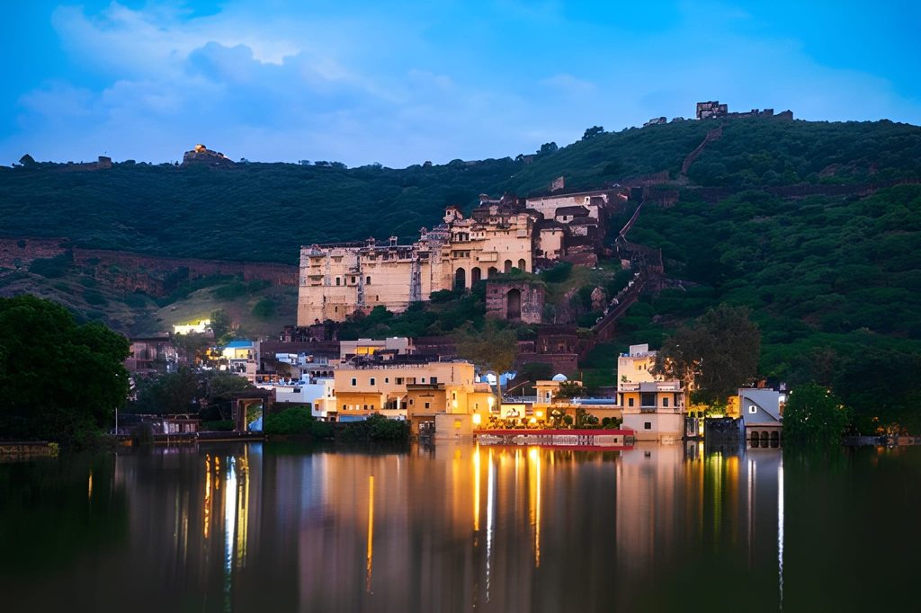 Nighttime view of Taragarh Fort and Garh Palace ruins in Bundi, Rajasthan, illuminated and reflected in the lake below, highlighting Underrated Places in India.