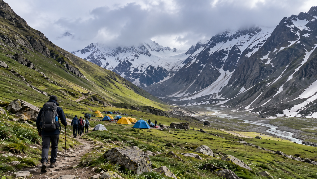 Hampta Pass Trek in Himachal Pradesh with hikers approaching a colorful mountain campsite surrounded by green alpine meadows, snow-covered peaks, and a winding glacial stream.