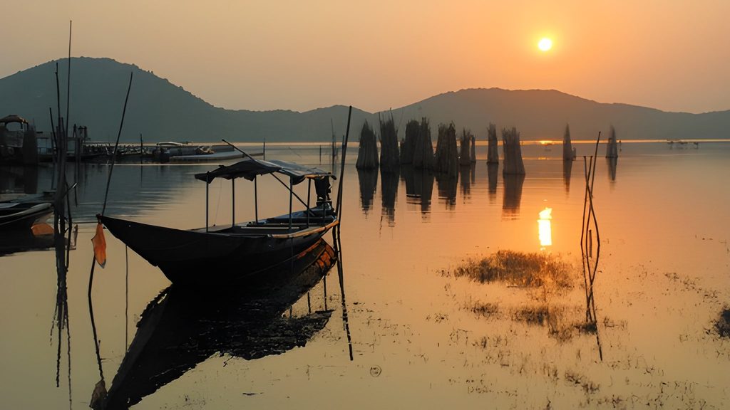 A boat docked in the still waters of Chilika Lake, Odisha, at sunset, with hills and fishing nets visible, showcasing Underrated Places in India.