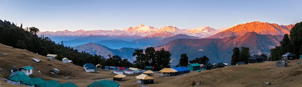 Panoramic view of a campsite in Chopta, Uttarakhand, nestled among hills with snow-capped Himalayan peaks glowing at sunrise, one of the Underrated Places in India.