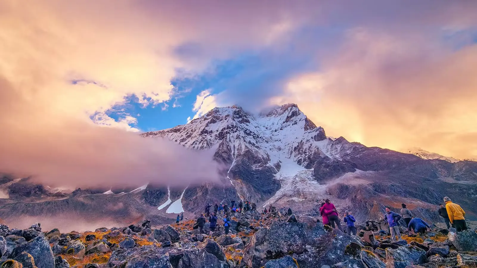 Trekkers exploring the rocky Goecha La Trek in Sikkim with dramatic snow-covered Himalayan peaks, misty clouds, and colorful sunrise skies.