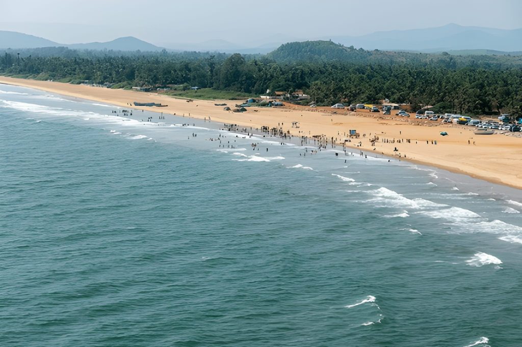 Aerial view of the long, sandy beach and blue ocean at Gokarna, Karnataka, backed by palm trees and hills, one of the Underrated Places in India.