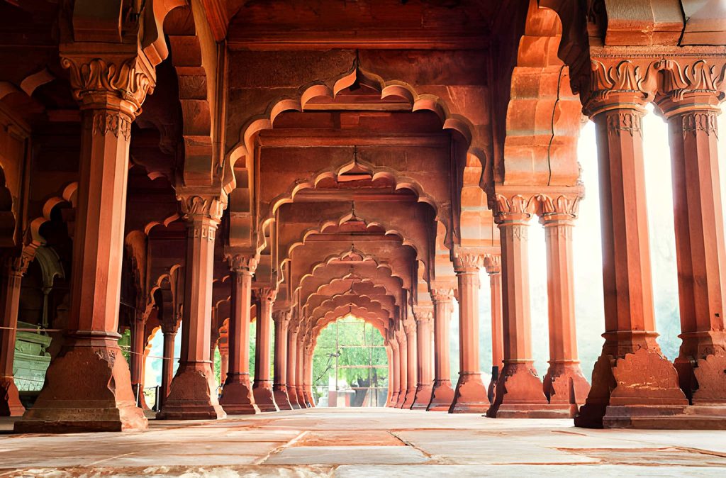 Historic red sandstone arches and carved pillars inside the Red Fort in Delhi, showcasing traditional Mughal architecture and a long symmetrical corridor.